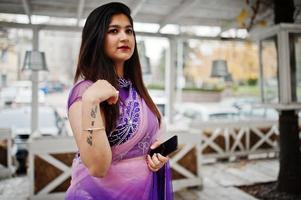 Indian hindu girl at traditional violet saree posed at street against wooden terrace. photo