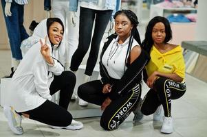 Three afican american women in tracksuits shopping at sportswear mall against mannequin. Sport store theme. photo