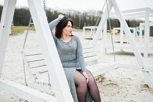 Portrait of brunette girl in gray dress sitting at white wooden construction. photo