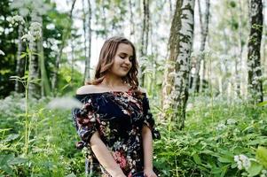 Portrait of a fabulous young girl in pretty dress with stylish curly hairstyle posing in the forest or park. photo