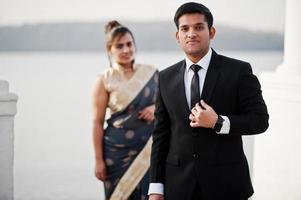 Elegant and fashionable indian friends couple of woman in saree and man in suit posed on the shore of the marina. photo