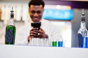 camarero afroamericano en el bar haciendo cócteles en tomas y tomando fotos en el teléfono. preparación de bebidas alcohólicas.
