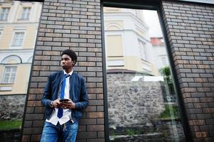 African man wear in tie and casual outfit posing outdoor with mobile phone. photo