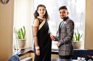 Lovely indian couple in love, wear at saree and elegant suit, posed on restaurant against window. photo