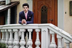 Elegant indian macho man model on suit and pink tie leaned on the railing. photo