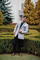 Stylish indian man with bindi on forehead and glasses, wear on suit posed outdoor against green bushes at park. photo