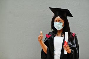 Young female african american graduate student wears a protective mask against coronavirus. Concept of graduation ceremony, quarantine. photo