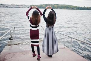 Portrait of back two young beautiful indian or south asian teenage girls in dress show heart by hands. photo