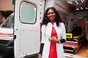 African american female paramedic standing in front of ambulance car. photo