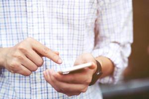 Young man wear plaid shirt.  close up hand using on cell phone during rest on sofa. sitting in watching message on mobile smart phone during break relax. soft focus. photo