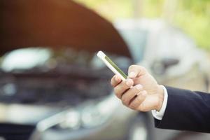 close up young business man hand using a mobile smart phone call a car mechanic ask for help assistance because car broken on the roadside. blank if empty screen. photo