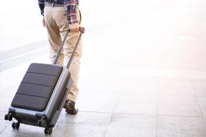 empresario caminando fuera del edificio de transporte público con equipaje en hora punta. viajero de negocios tirando de la maleta en la moderna terminal del aeropuerto. viaje de negocios de equipaje. foto