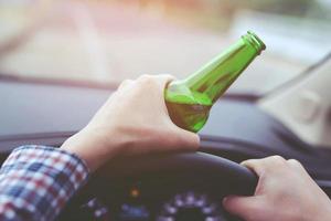 close up hand Drunk young man while driving a car with a bottle of beer. Don't drink and drive concept. Driving while intoxicated the danger may be a death. photo