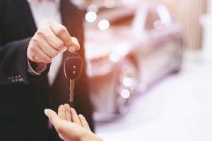 la llave del auto, el hombre de negocios entrega la llave del auto a la otra mujer en el fondo del auto. foto