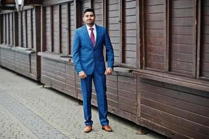 Elegant indian fashionable man model on suit posed against wooden stalls. photo
