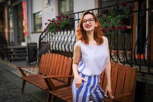 atractiva mujer pelirroja con anteojos posando en la calle de la ciudad de la primavera. foto