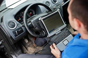 Car repair and maintenance theme. Electric mechanic in uniform working in auto service, making car diagnostics using obd device with laptop. photo