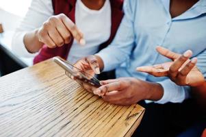 Three african american girls sitting on the table of caffe and looking on mobile phone. photo