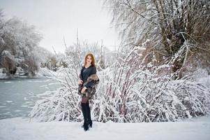 Red haired girl in fur coat walking at winter snowy park. photo