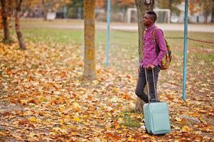 African american man in checkered shirt, with suitcase and backpack. Black man traveler at autumn park. photo