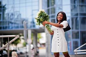 Beautiful african american girl holding bouquet of white roses flowers on dating in the city. Black businesswoman with bunch of flowers. photo