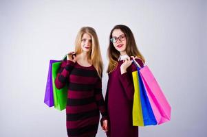 dos hermosas amigas con vestidos de cereza posando con bolsas de compras multicolores en el estudio. foto