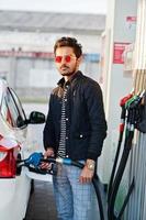 hombre del sur de asia o hombre indio repostando su auto blanco en la gasolinera. foto