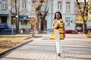 Stylish african american women in yellow jacket posed on street at sunny day with mobile phone at hand. photo