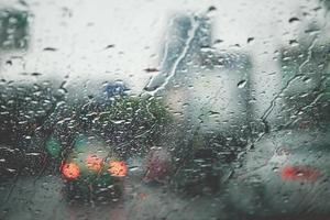 gotas de lluvia lloviznan en el parabrisas de cristal por la noche. calle bajo la fuerte lluvia. Bokeh luz trasera y semáforos en la ciudad. conduzca el automóvil con cuidado, camino resbaladizo. enfoque suave. foto