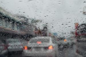 Drops Of Rain Drizzle on the glass windshield in the evening. street in the heavy rain. Bokeh Tail light and Traffic lights in city. Please drive  car carefully, slippery road. soft focus. photo