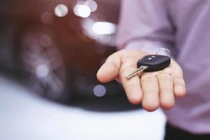 la llave del auto, el hombre de negocios entrega la llave del auto al otro hombre en el fondo del auto. foto