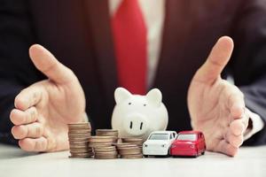 Business man in suit hand holding model of toy car white on over a lot money of stacked coins insurance, loan and buying car finance concept. buy and installments down payment a car. Piggy Bank saving photo