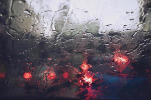 gotas de lluvia lloviznan en el parabrisas de cristal por la noche. calle bajo la fuerte lluvia. Bokeh luz trasera y semáforos en la ciudad. conduzca el automóvil con cuidado, camino resbaladizo. enfoque suave. foto