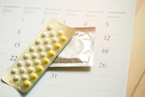 Contraceptive control pills and condom on date of calendar calculate date Control the birth rate. table wood background. health care and medicine, contraception concept. empty space for text. photo