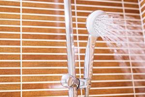 el cabezal del grifo de la ducha en el baño con una gota de agua salpicada corriendo. Fondo vintage de estilo de azulejo de pared interior. foto