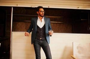 Handsome well-dressed arabian man smoke cigar with glass of whiskey at balcony of pub. photo