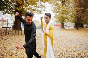 Two indian stylish mans friends in traditional clothes dancing outdoor. Navaratri dance. photo