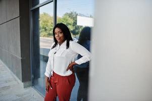 Formally dressed african american business woman in white blouse and red trousers. Successful dark skinned businesswoman. photo