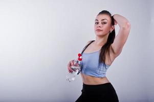 Wet cheerful attractive young fitness woman in top and black leggings with jump rope and bottle of water isolated over white background. photo