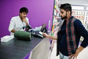 Indian man customer buyer pay for his new smartphone for seller by credit card at mobile phone store. South asian peoples and technologies concept. Cellphone shop. photo