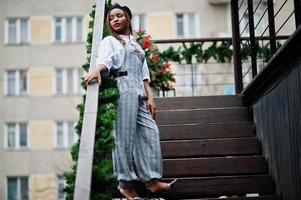 African american woman in overalls and beret posed in outdoor terrace with christmas decorations garland. photo