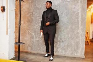 Strong powerful african american man in black suit and turtleneck with elephant tusk. photo