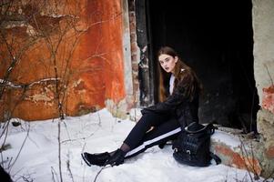 Fashionable long legs brunette model in long black cloak posed outdoor at winter day against old grunge wall. photo