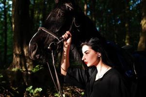 Mystical girl wear in black with horse in wood. photo