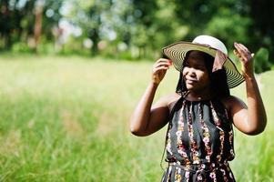 Portrait of gorgeous african american woman 20s in summer hat posing at green grass in park. photo