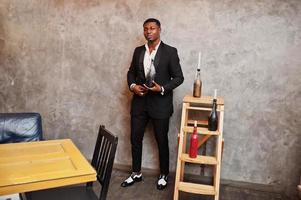 Strong powerful african american man in black suit posed against gray wall with candle decorations. photo