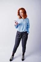 retrato de una joven empresaria pelirroja con camisa azul y pantalones enviando mensajes de texto por teléfono. foto