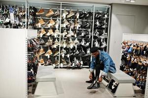 Stylish casual african american man at jeans jacket and black beret at clothes store trying new footwear. photo