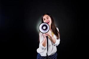 Portrait of a young woman in blue trousers and white blouse posing with megaphone in the studio. photo