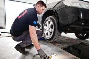 Car repair and maintenance theme. Mechanic in uniform working in auto service, checking tyres. photo